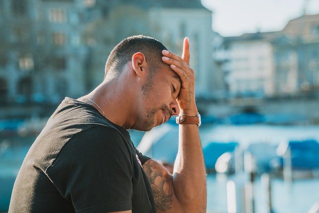 A tired man holding his head with his left hand while his eyes are closed.