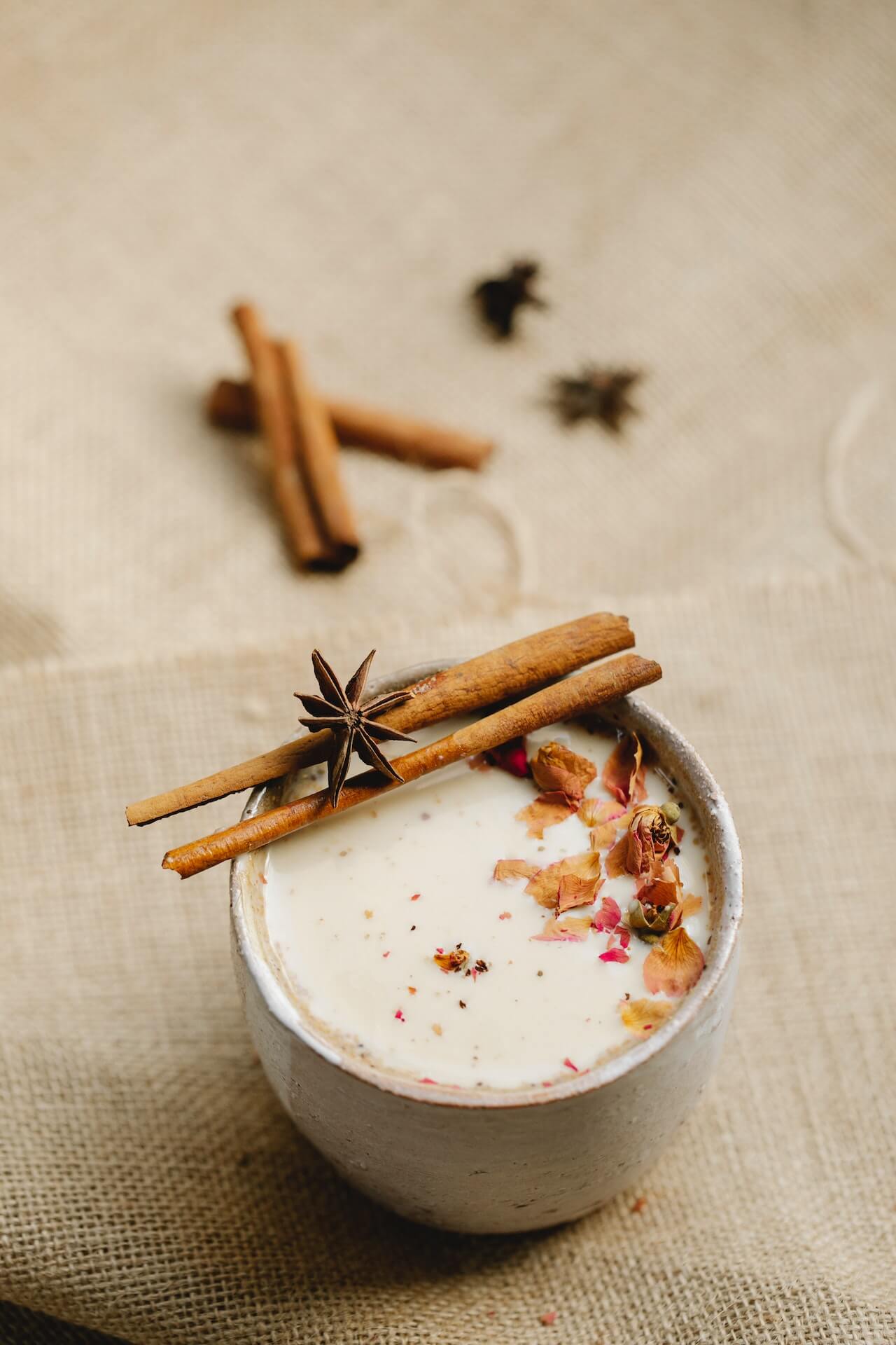 A cup filled with a white natural Morning Recovery Hangover Drink with two pieces of cinnamon laid on top.