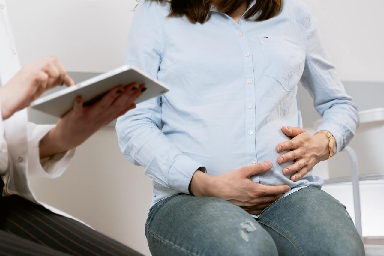 A pregnant woman holding and protecting her belly while receiving the results from the doctor.